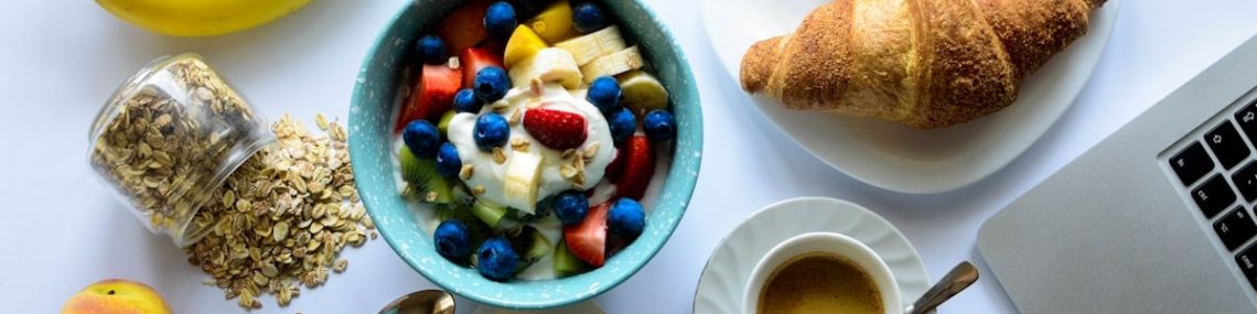 top view of strawberry and berries parfait in bowl near croissant and laptop